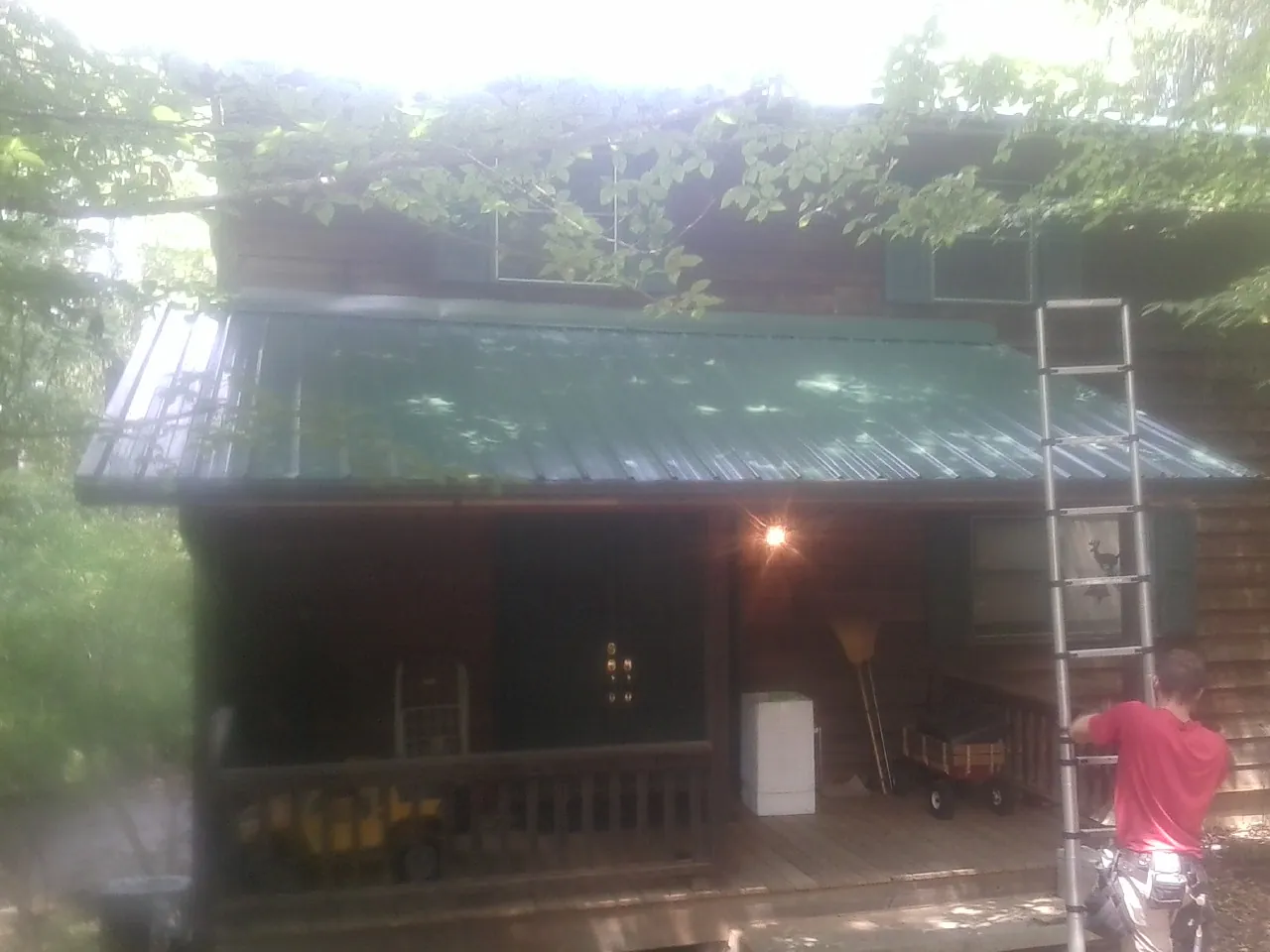 Worker on a ladder at the green porch roof of a wooded cabin in Avon